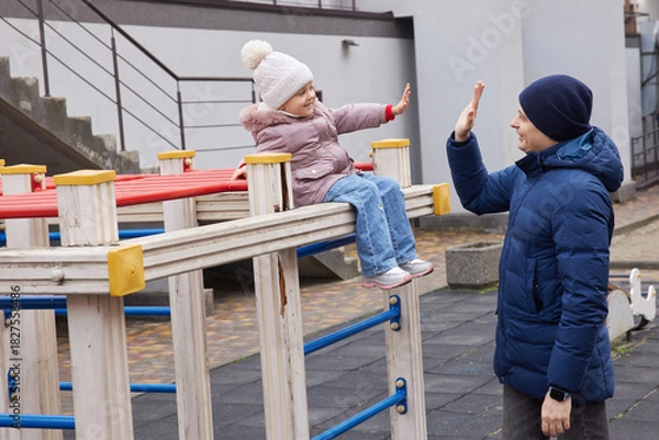 Fototapeta Father and daughter bonding, giving a high five, and playing outdoors during winter