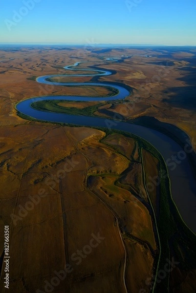 Obraz Aerial view of a meandering river through a dry landscape under a clear blue sky