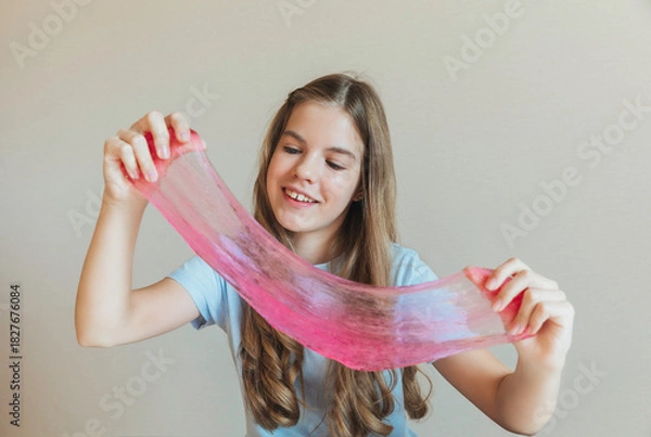 Fototapeta Close-up of hands stretching bright pink slime towards the camera, with a smiling girl in the background. Sensory toy