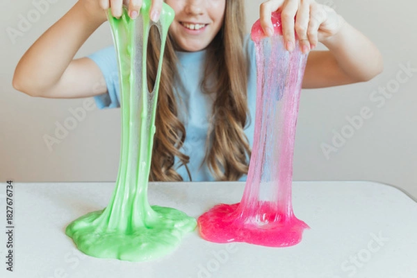 Fototapeta Girl stretching bright green and pink slime simultaneously, showcasing two colors. Fun dual sensory play activity