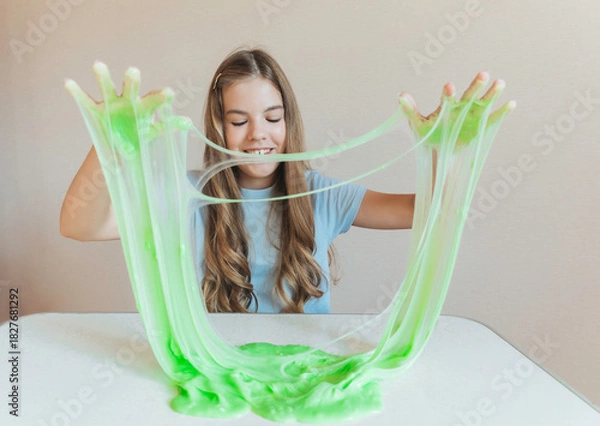 Fototapeta Smiling girl holding and stretching lime green slime wide, showcasing its elasticity and stringy texture. Fun sensory play