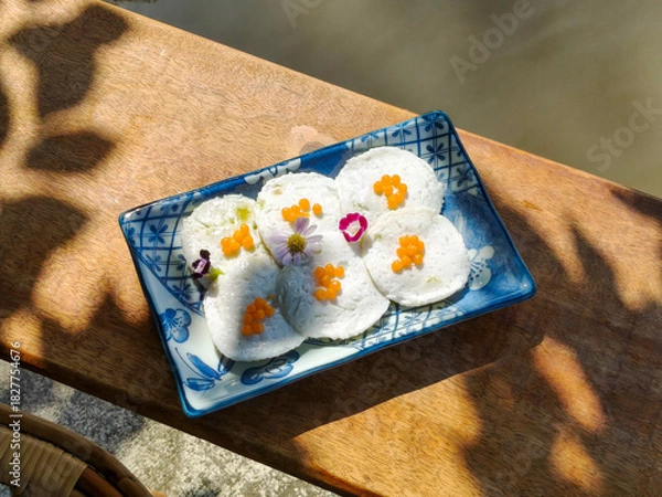 Fototapeta Steamed Coconut Custard or Kanom Tuay. Thai dessert made from rice flour, coconut milk and sugar steamed in small ceramic cups with pandan leaves and coconut milk poured over it. Top view