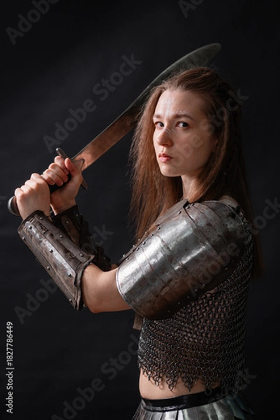 Fototapeta Portrait of a young woman, fantasy warrior in armor with a sword in her hands isolated on a dark background.