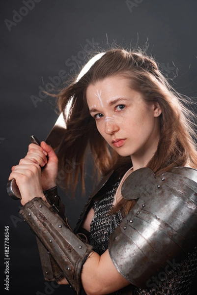 Fototapeta Portrait of a young woman, fantasy warrior in armor with a sword in her hands isolated on a dark background.