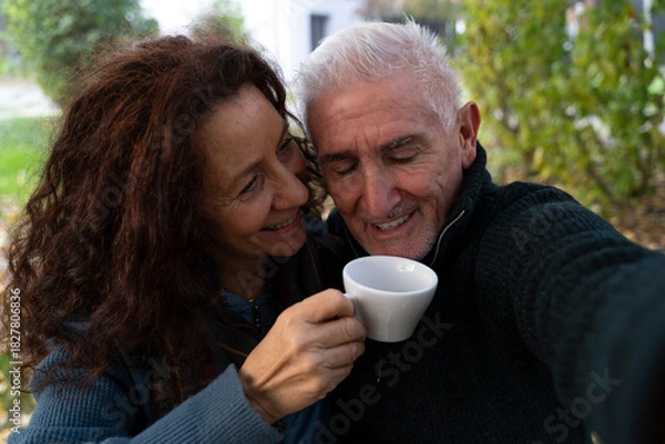 Fototapeta Happy senior couple smiling, drinking coffee, and taking a selfie in a park