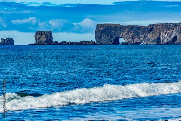 Fototapeta Afternoon waves crash below the deep blue sky and the magnificent Dyrhólaey arch near Cape Vik Southern Iceland