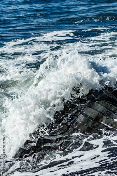 Fototapeta Midday waves clash with basalt bones along the rugged edge of Black Beach in Southern Iceland’s volcanic embrace