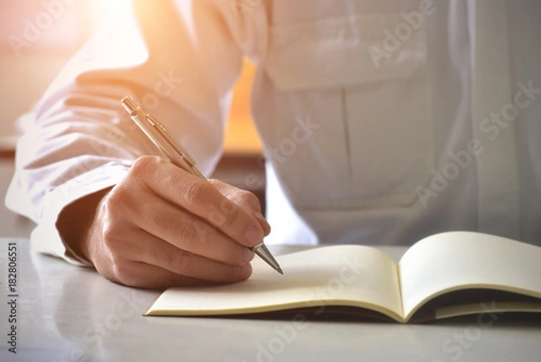 Fototapeta Close up hand writing in an agenda on a desk at home or office