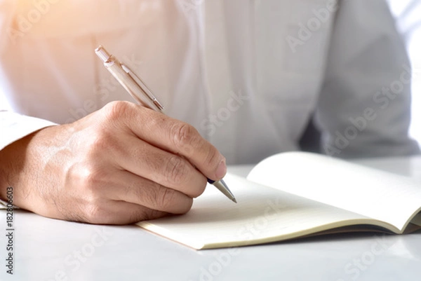 Fototapeta Close up hand writing in an agenda on a desk at home or office
