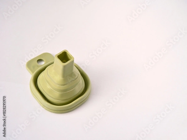 Fototapeta A flexible green rubber folding funnel isolated on a white background. A practical contemporary household item.
