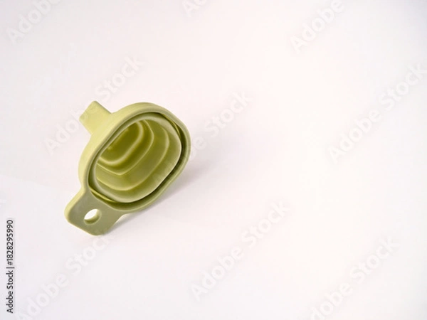Fototapeta A flexible green rubber folding funnel isolated on a white background. A practical contemporary household item.