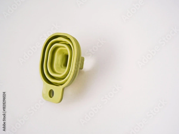 Fototapeta A flexible green rubber folding funnel isolated on a white background. A practical contemporary household item.