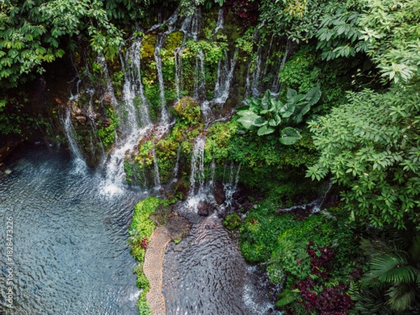 Fototapeta Tropical waterfall cascading over mossy rocks surrounded by jungle foliage