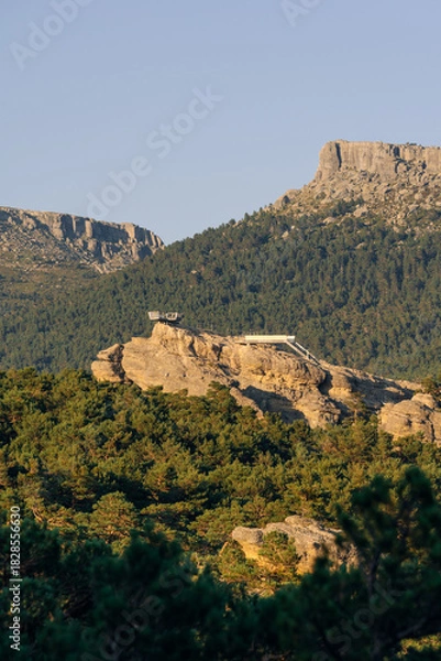 Fototapeta Walkways among rock formations and pine trees with the peaks of Urbion in the background in the Castroviejo nature reserve, in Duruelo de la Sierra, Soria, Castile and Leon, Spain.