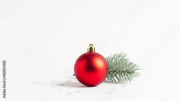 Fototapeta A single, isolated, matte red christmas bauble with a pine tree sprig and scattered snowflake confetti on a clean white background.