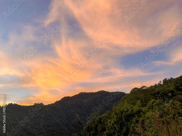 Fototapeta Spectacular sunrise sky with wispy pink and orange clouds above the dense, dark green mountain range in Wulai, New Taipei City, Taiwan, highlighting natural beauty.