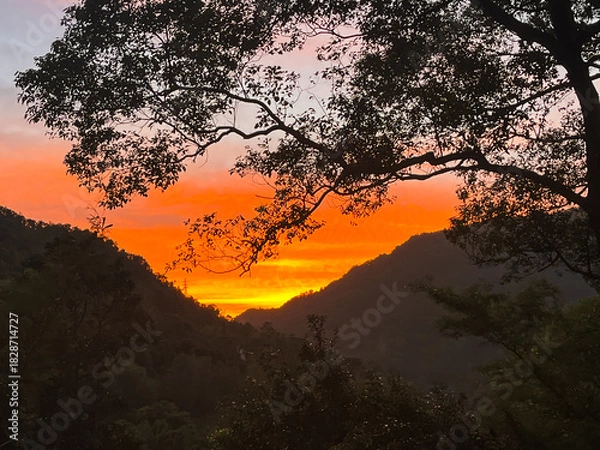Obraz Striking orange and yellow sunrise illuminates the sky above a dark mountain valley silhouette in Wulai, New Taipei City, Taiwan, creating a dramatic and powerful scene.