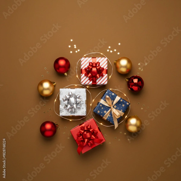 Fototapeta Christmas Flat Lay Composition with Assorted Gift Boxes, Red and Gold Ornaments, Fairy Lights, and Glitter on a Warm Brown Background – Holiday Shopping, Giving, and Festive Season Concept