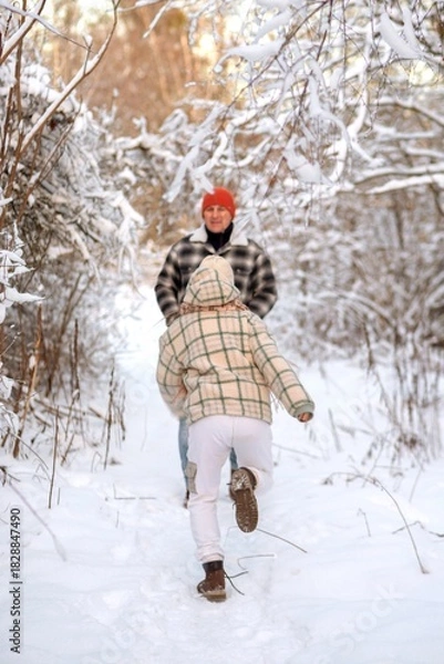 Fototapeta Father and daughter playing and enjoying the snow in a winter forest. Concept of family joy, warm emotions, childlike happiness, and fun winter activities outdoors.