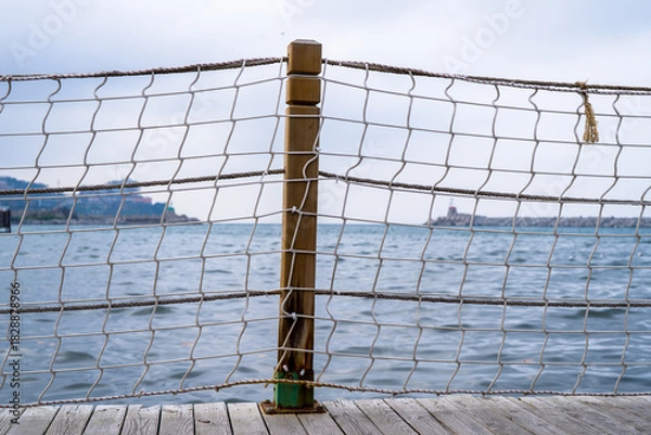 Fototapeta Wooden Post With Rope Netting At Pier Over Calm Water – A Coastal Scene