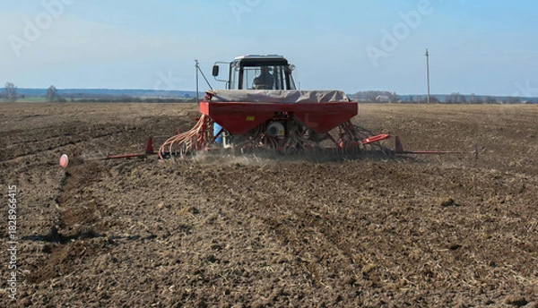 Obraz Farmer uses tractor to plant seeds in a freshly plowed field during early spring