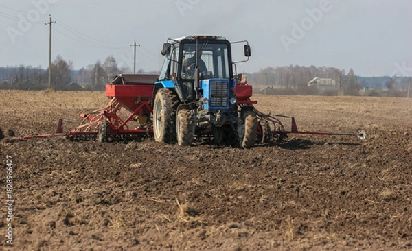 Fototapeta Farm tractor plowing a field on a sunny day in rural countryside