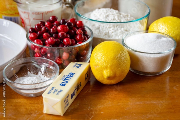 Fototapeta Homemade cranberry lemon cake ingredients: flour, butter, fresh cranberries, and lemon on a rustic dark wood cutting board. Natural light.