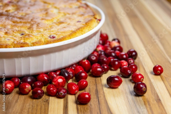 Fototapeta Rustic close-up of a freshly baked cranberry cake showing the golden, cracked crust and edge of the dish on a dark wood board. Cozy homemade food.