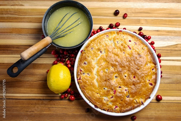 Fototapeta Overhead flat lay of whole cranberry lemon cake with lemon slices, fresh cranberries, and clear bowl of drizzle. Homemade holiday recipe.