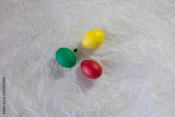 Fototapeta Brightly colored Easter eggs – various colors - green, yellow, red, blue – arranged on crumpled white paper. The eggs are smooth and shiny, ready for decoration or display at Easter