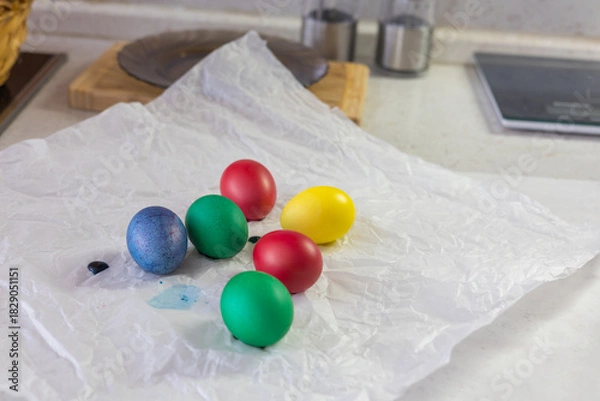 Fototapeta Brightly colored Easter eggs – various colors - green, yellow, red, blue – arranged on crumpled white paper. The eggs are smooth and shiny, ready for decoration or display at Easter