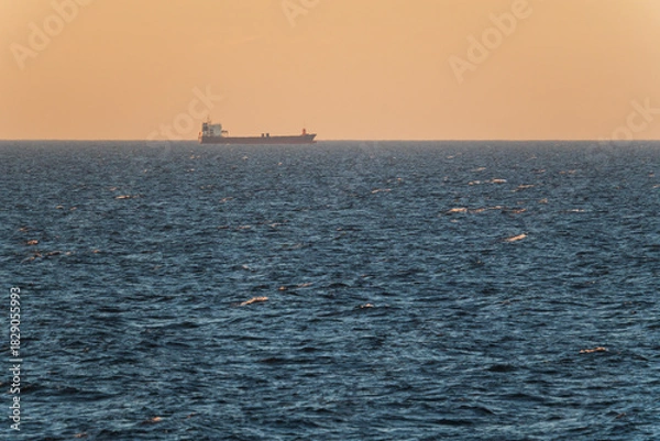 Fototapeta Silhouette of a large cargo ship sailing on the horizon of the Baltic Sea during a golden sunset evening