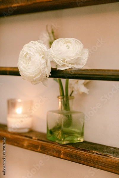 Fototapeta White flowers in a glass vase with candles creating a cozy atmosphere in a rustic setting