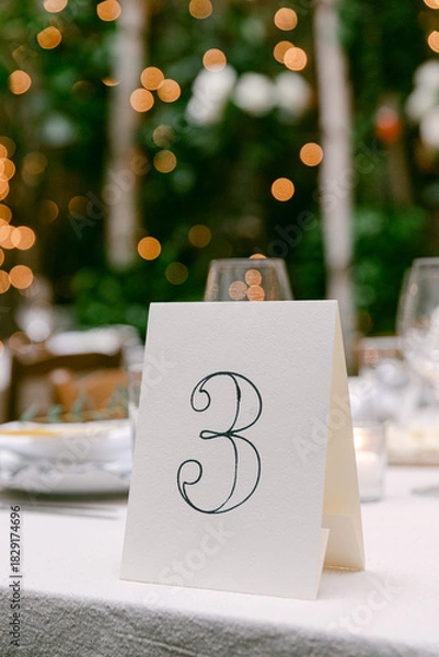 Fototapeta Elegant table number three set against a beautiful bokeh background at an outdoor event