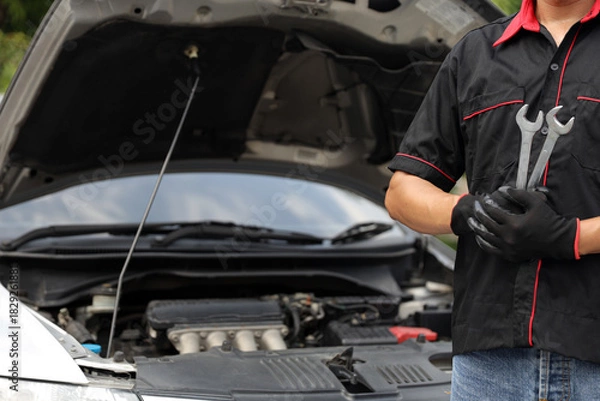 Fototapeta Car mechanic holding wrench for fix service repairing change spare part engine problem or insurance support or range of car check or training workshop and auto care maintenance servicing concepts.