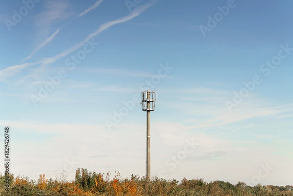 Obraz Concrete communication tower stands tall against autumn trees and a beautiful blue sky with airplane contrails