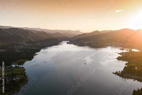 Fototapeta Aerial view of Colibița Lake in the Carpathian Mountains of Romania during a warm summer sunset. Golden light over the water and surrounding hills. Travel to Romania, Transylvania.