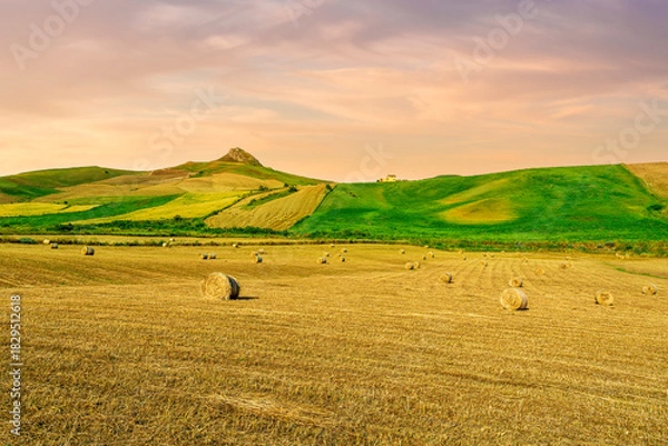 Fototapeta beautiful summer golden field among green hills and mountains with yellow hay stacks and scenic landscape on background. Agricultural landscape of rustic farmland.