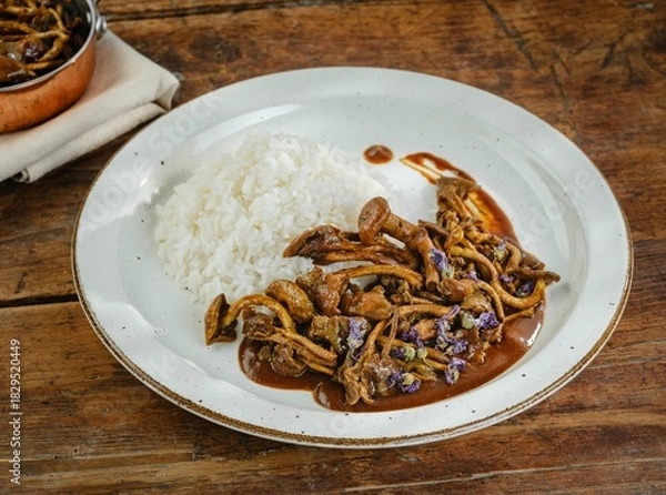 Fototapeta A plate of flavorful meat and mushrooms sits beside a mound of fluffy white rice. The setting is warm and inviting, showcasing a cozy meal among friends or family