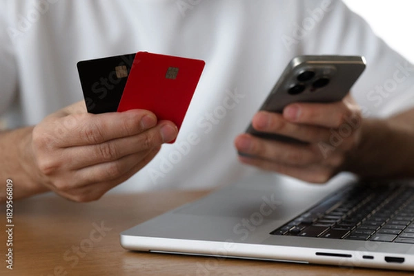Fototapeta Man holds smartphone and credit cards next to laptop
