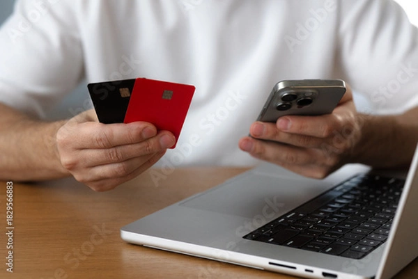 Fototapeta Online sevices. Man holds smartphone and credit cards next to laptop close-up