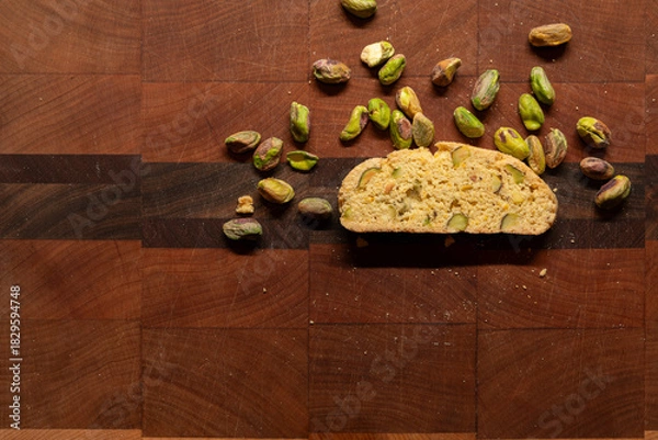 Fototapeta Twice baked biscotti cookie on an end grain cutting board, surrounded by pistachio nuts and crumbs with copy space