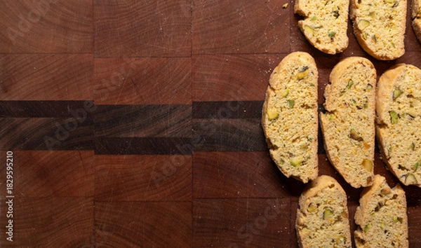 Fototapeta Batch of prange and pistachio, freshly baked biscotti on a wooden cutting board with copy space