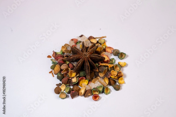 Fototapeta A macro photograph of a single dried Star Anise fruit resting on a pile of smaller, brightly colorized botanical seed capsules and clear crystalline material on a bright white backgr