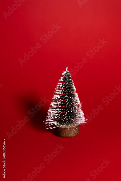 Obraz A small decorative Christmas tree with a wooden base, covered in white glitter, standing on a bright red background.