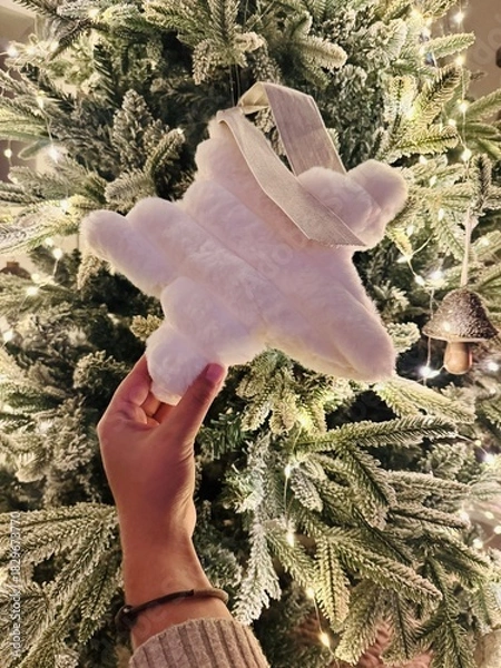 Obraz Hand Decorating Christmas Tree with Star Topper and Fireplace Burning Behind – Warm Festive Setting