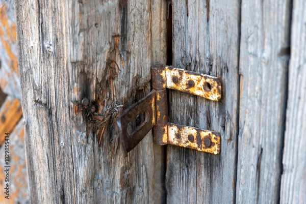Obraz Close-up of a rusty metal latch on old weathered wooden doors, originally used to lock and secure the wooden entrance.