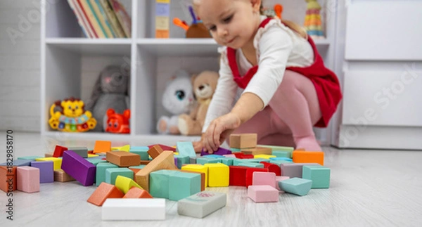 Obraz Little girl building a tower with colorful wooden blocks on the floor.