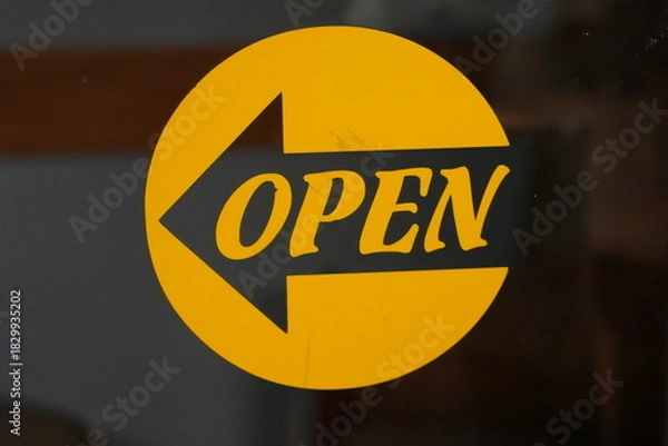 Fototapeta Vibrant Yellow Open Sign with Arrow Pointing Left on a Glass Door