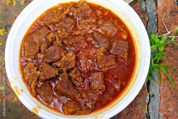 Fototapeta Close-up of finished beef goulash with tender meat chunks in glossy red sauce served in white bowl. Represents comfort food, Hungarian stew presentation, traditional meat dish, and warming winter food